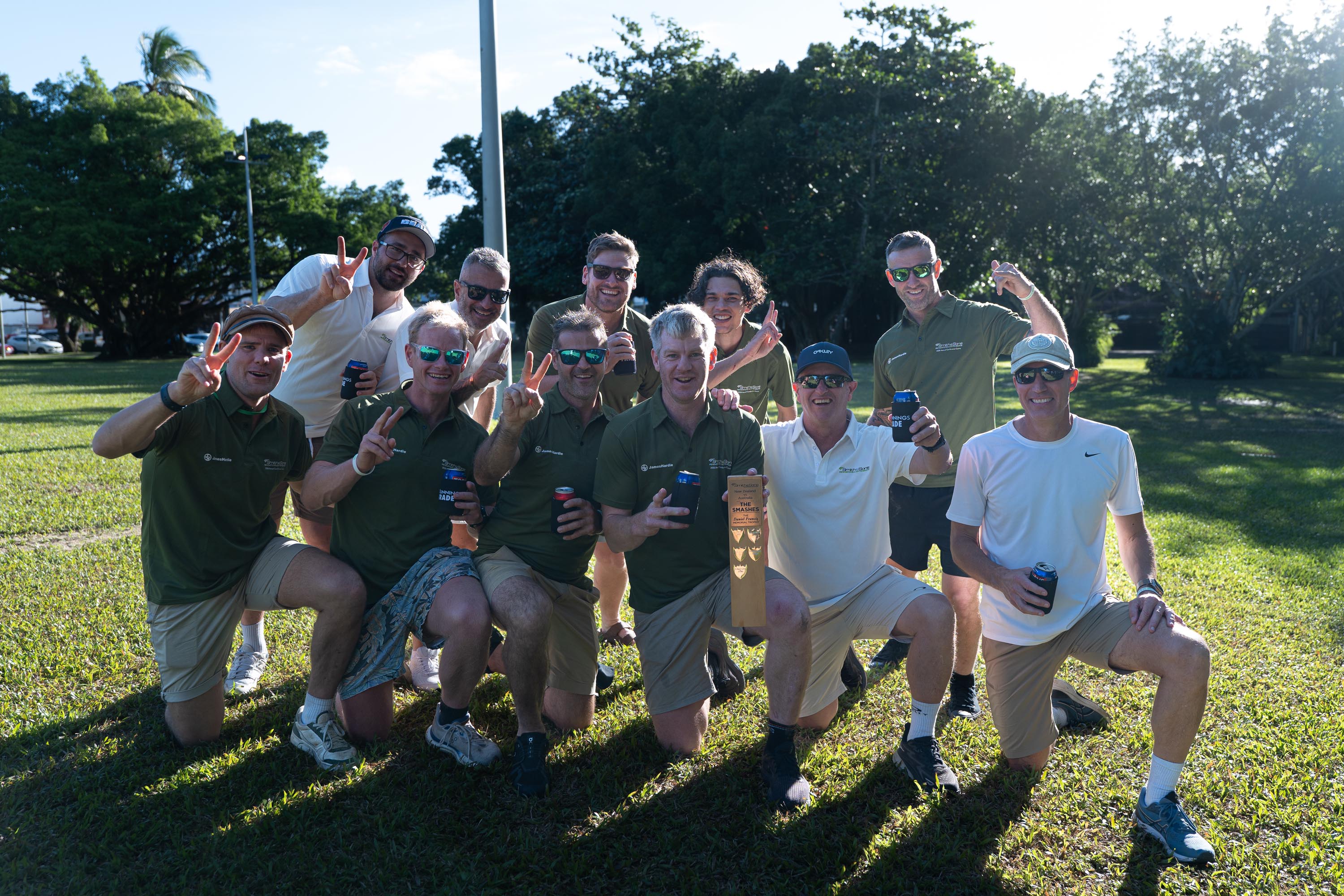 Smith & Sons team in olive polos kneeling on the grass holding The Smashes memorial trophy