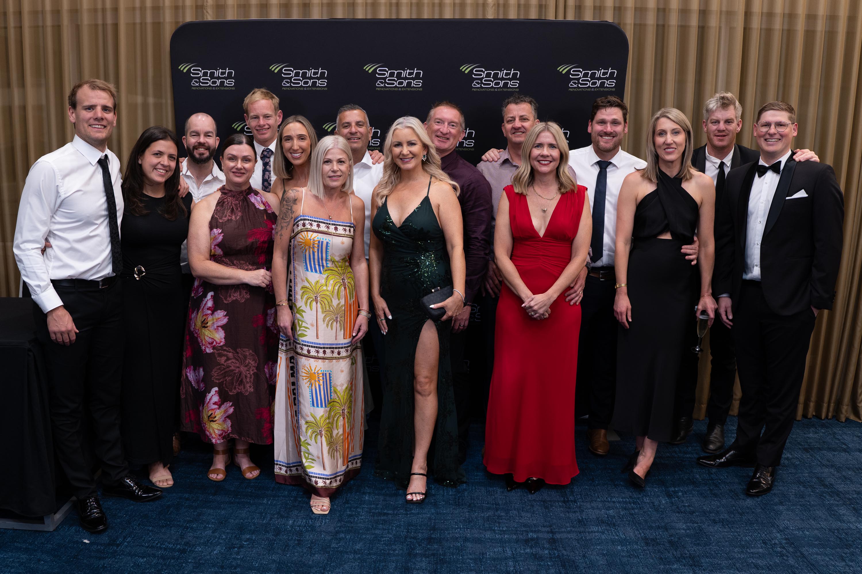 Team members in black-tie attire posing in front of the Smith & Sons media wall