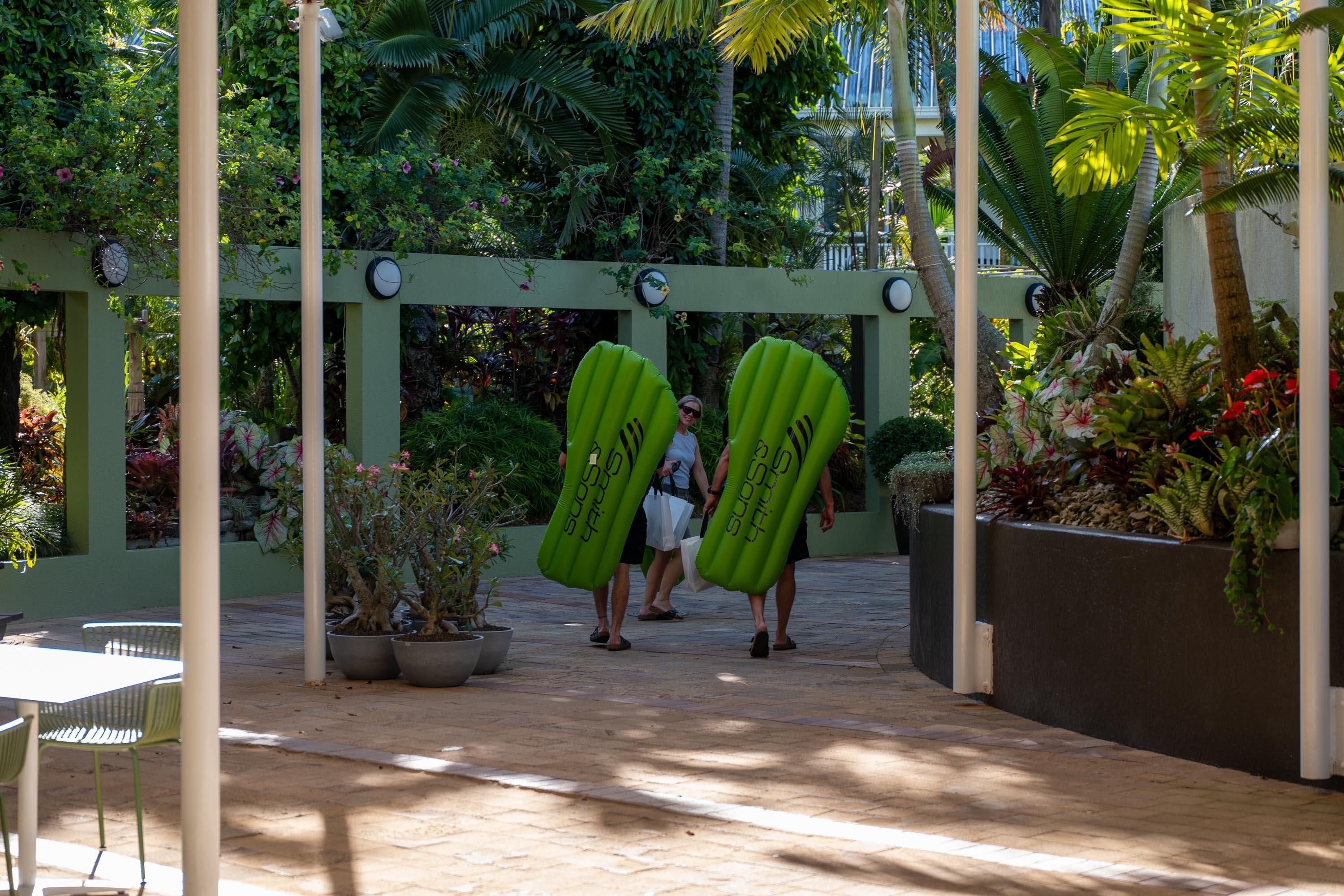 Two attendees carrying green Smith & Sons pool mats through the tropical resort gardens
