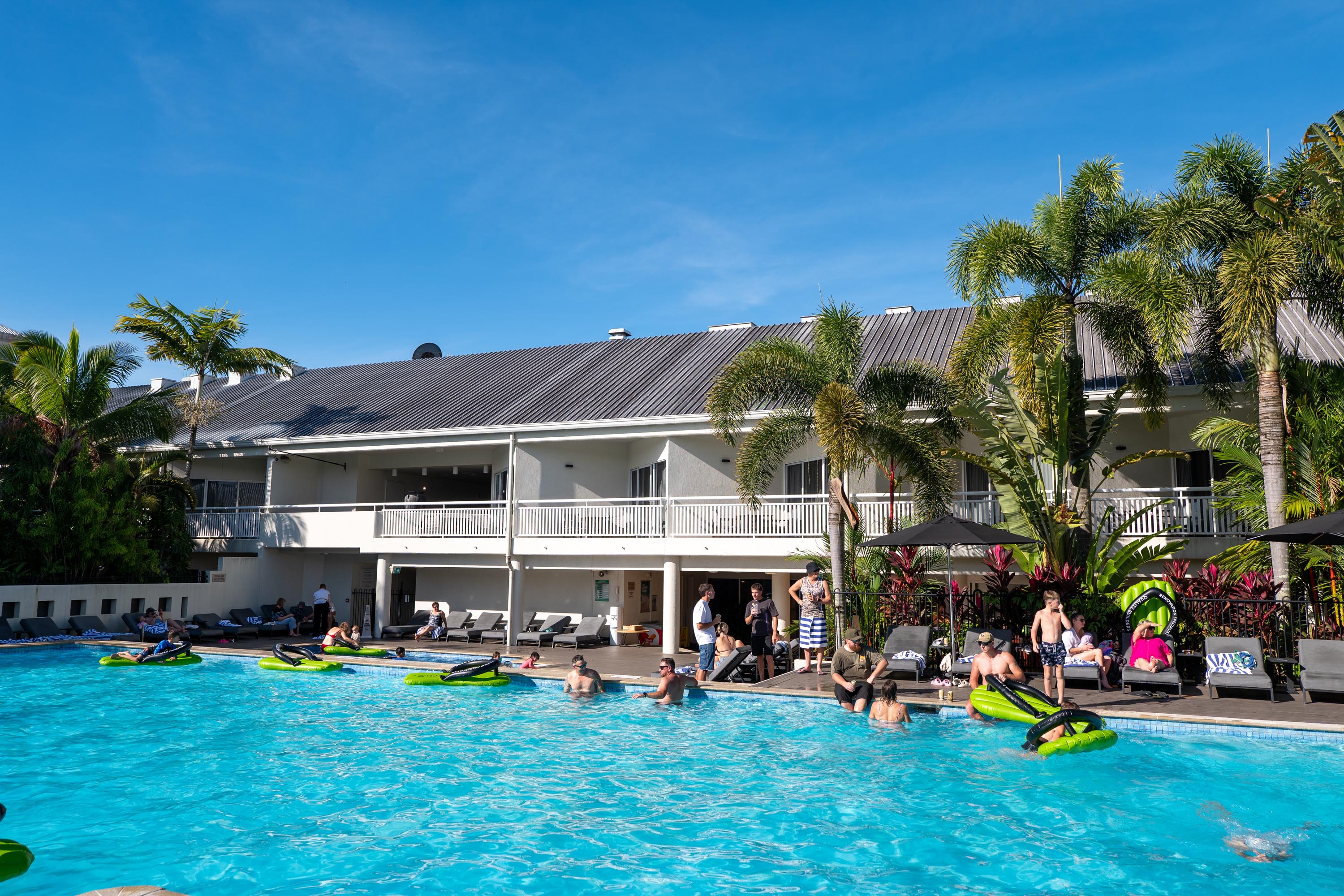 Resort pool ringed by palm trees with attendees floating on green Smith & Sons inflatables