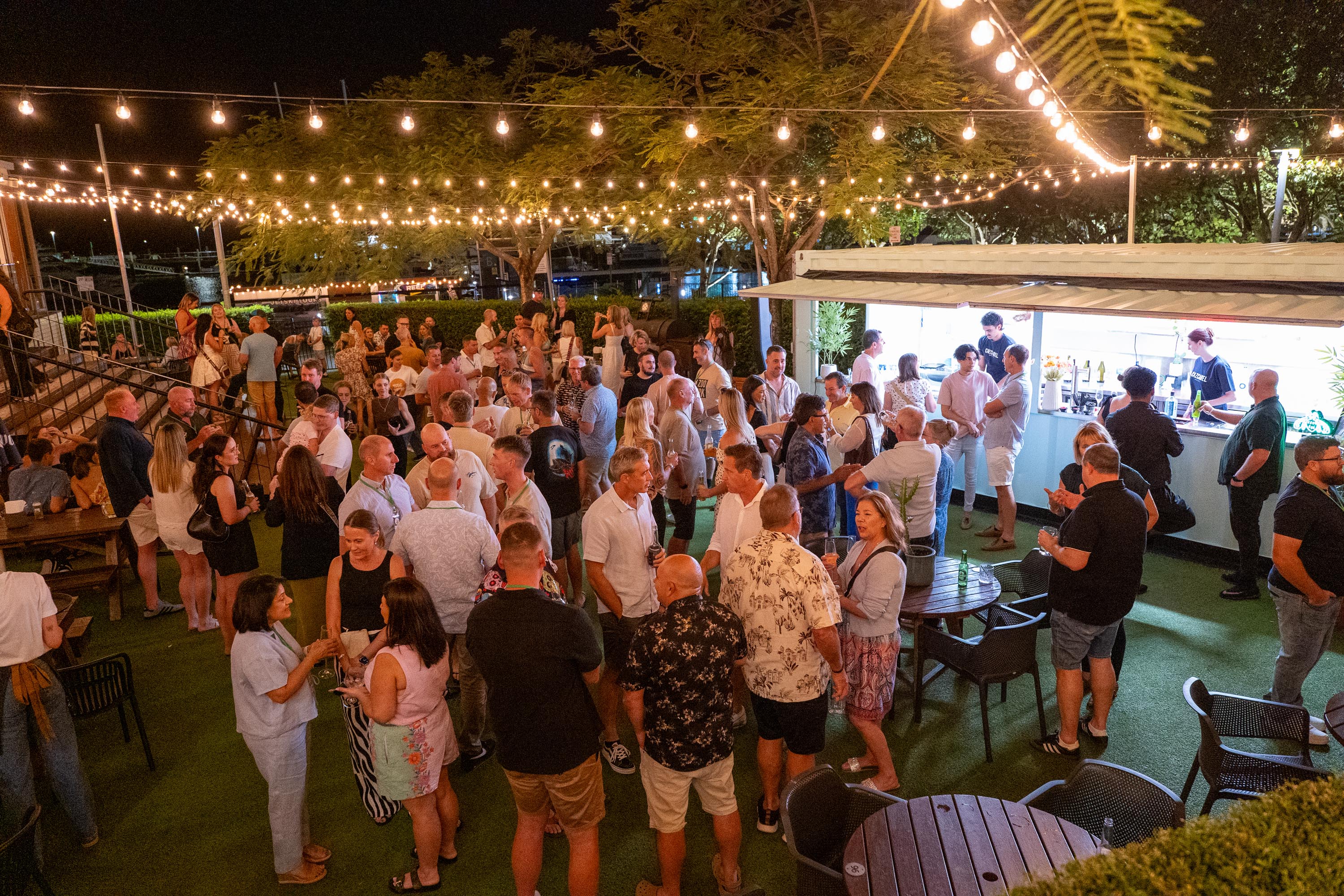 Guests mingling with drinks at an outdoor evening function under festoon lights