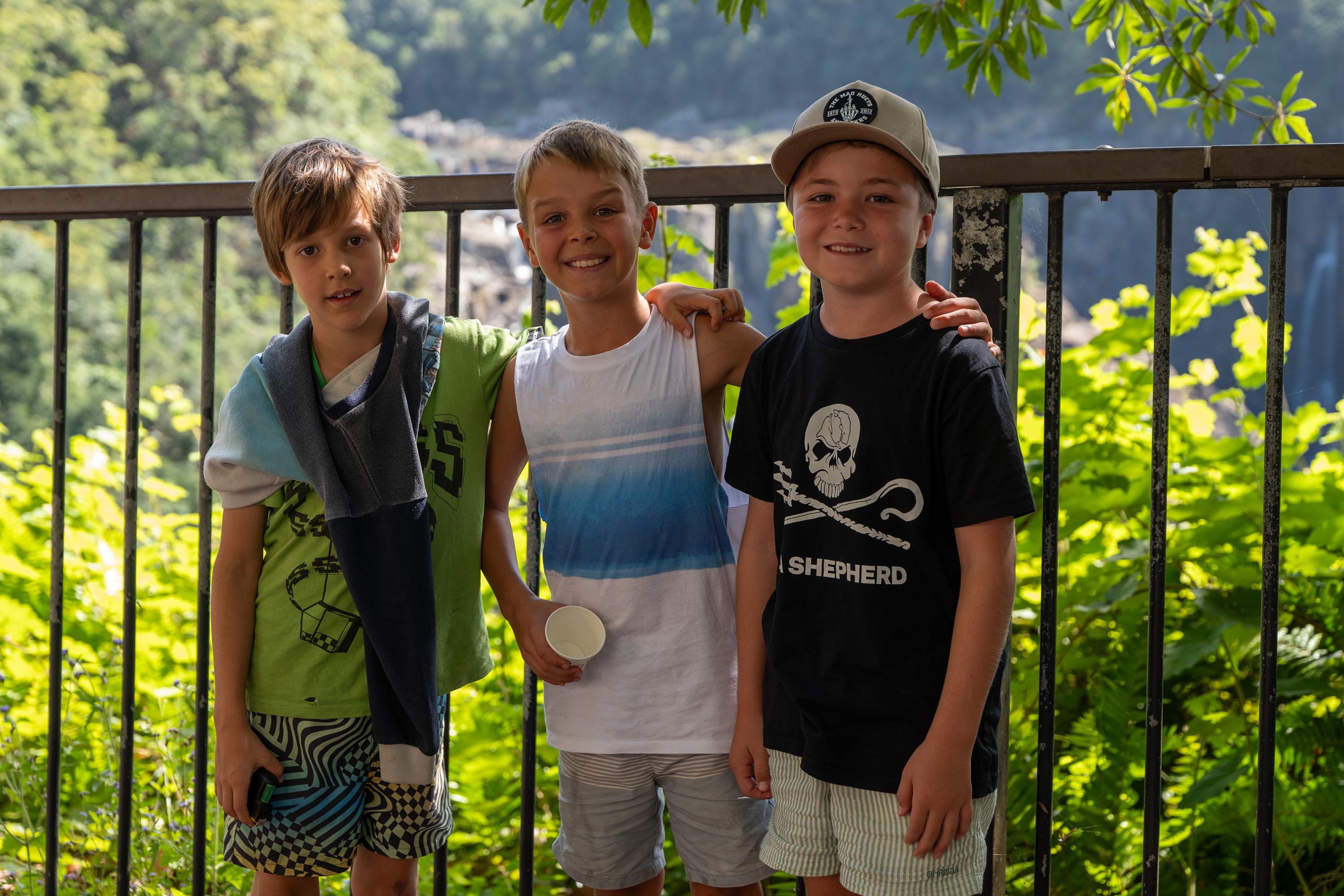 Three young boys posing at a lookout railing surrounded by lush greenery