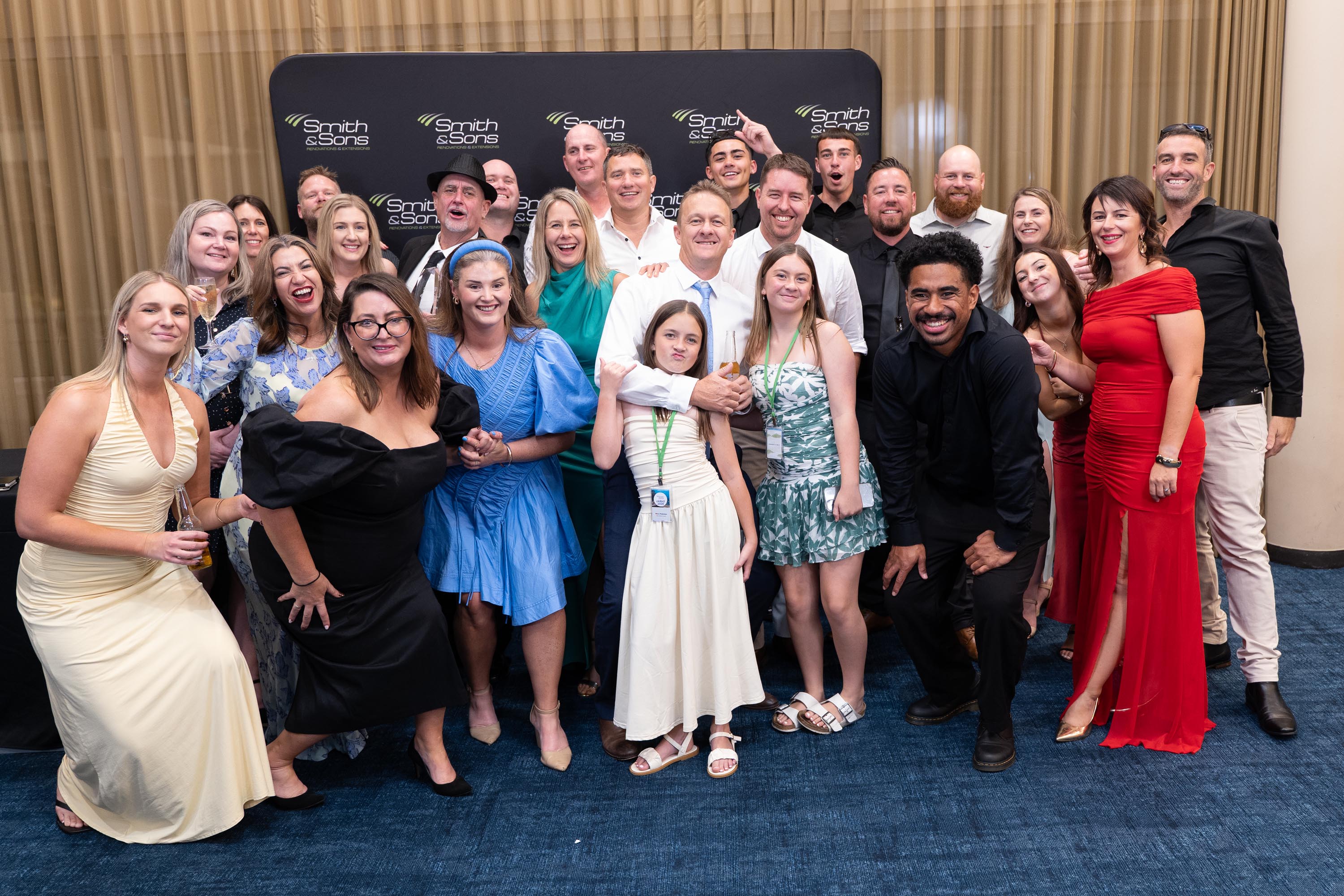 Large group of team members and families laughing together on the blue carpet